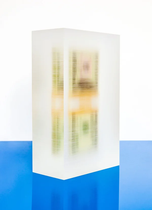 A frosted rectangular prism with embedded color, standing on a blue surface.