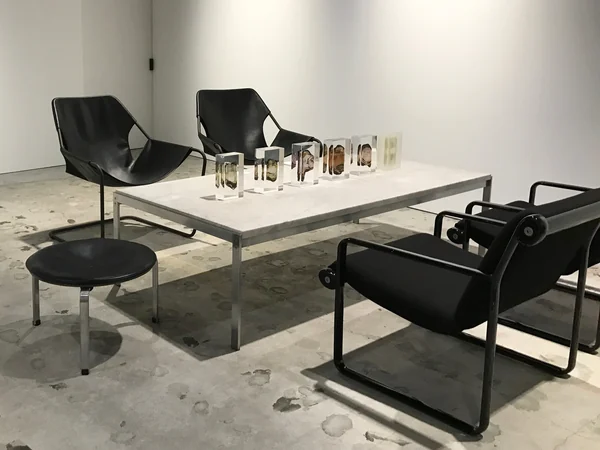 Translucent prism sculptures on a table surrounded by black chairs in a light-filled interior.