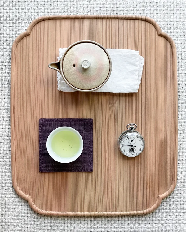 A teapot, cup of green tea and pocket watch arranged on a wooden tray.