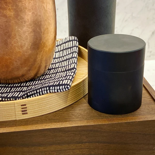 Tea objects and a black cylindrical canister on a wooden surface.